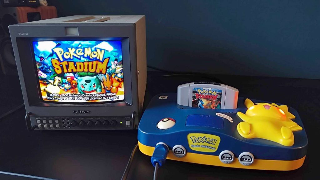 Pokemon Stadium on Sony PVM CRT next to Pikachu N64 console on black desk.