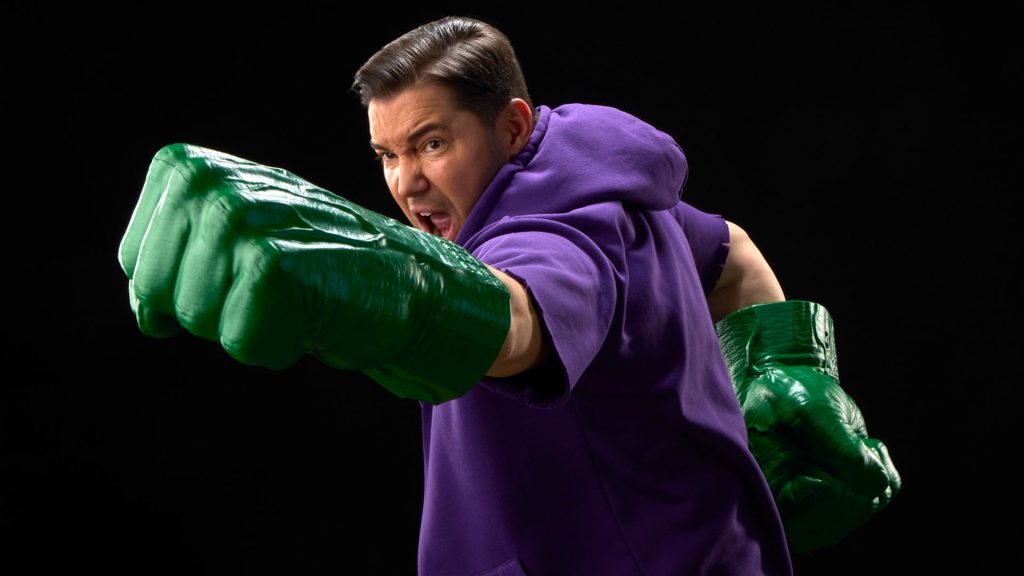 A man yells while punching with giant green Hulk Fists