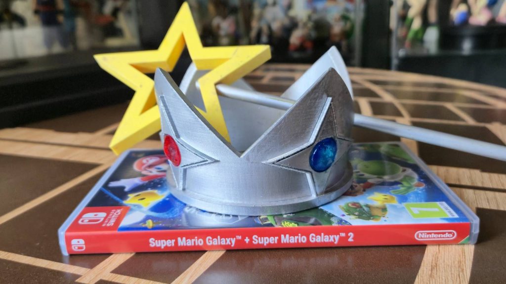Photo of a physical copy of Super Mario Galaxy + Super Mario Galaxy 2 sitting on a coffee table, with a replica of Rosalina's crown and wand sitting on top.