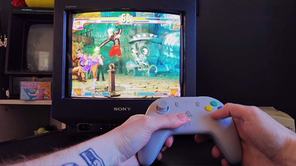 Retro Fighters StrikerDC being used with Sony Trinitron CRT TV and Sega Dreamcast to play Street Fighter Third Striker with Remi punching Chun-Li from above.
